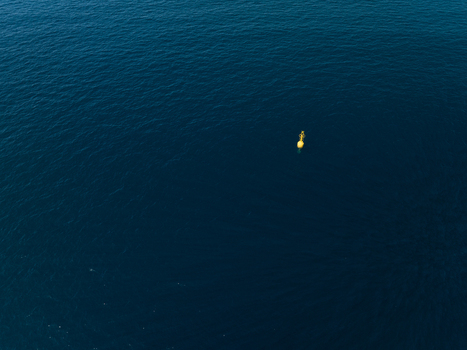 Aerial view of a yellow buoy floating in the deep blue waters of the Mediterranean Sea off the coast of Plemmirio Sicily Italy. Aerial view of a yellow buoy floating in the deep blue waters of the Mediterranean Sea off the coast of Plemmirio Sicily Italy.