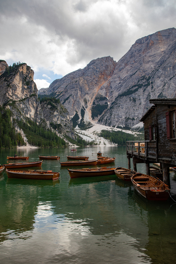View of wooden rowboats floating on the calm green waters of a mountain lake with the dramatic rocky peaks of the Dolomites in the background in Rocca Pietore Veneto Italy. View of wooden rowboats floating on the calm green waters of a mountain lake with the dramatic rocky peaks of the Dolomites in the background in Rocca Pietore Veneto Italy.