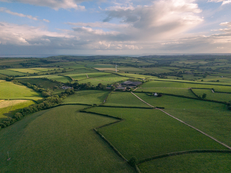Aerial view of lush green fields and hedgerows surrounding a farmstead in the rural landscape of Looe Cornwall United Kingdom. Aerial view of lush green fields and hedgerows surrounding a farmstead in the rural landscape of Looe Cornwall United Kingdom.