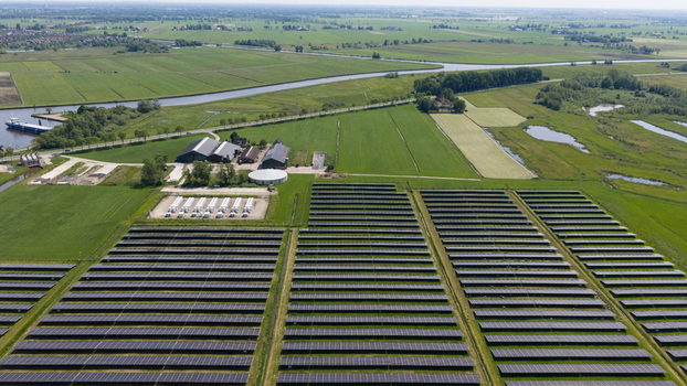 Aerial view of a large solar farm with rows of photovoltaic panels next to farm buildings and a canal in the flat rural landscape of Wanneperveen Overijssel Netherlands. Aerial view of a large solar farm with rows of photovoltaic panels next to farm buildings and a canal in the flat rural landscape of Wanneperveen Overijssel Netherlands.