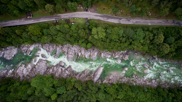 Aerial view of the turquoise Verzasca River flowing through rocky terrain and dense green forest with a parallel road in Verzasca Ticino Switzerland. Aerial view of the turquoise Verzasca River flowing through rocky terrain and dense green forest with a parallel road in Verzasca Ticino Switzerland.
