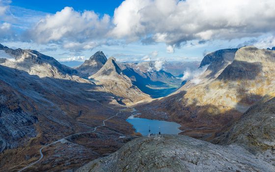 Aerial view of the rugged mountainous landscape featuring a winding road a serene alpine lake and dramatic peaks under a partly cloudy sky in Andalsnes More og Romsdal Norway.