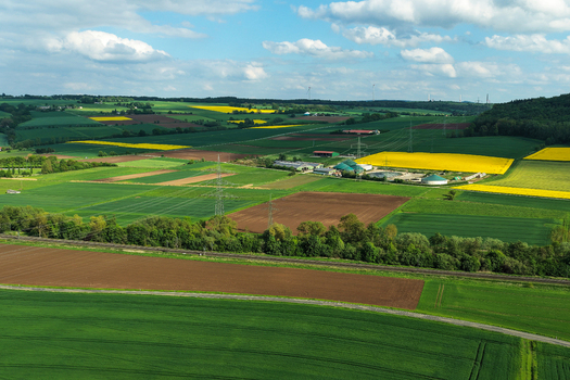 Aerial view of vibrant agricultural fields yellow rapeseed blossoms and a biogas plant nestled among rolling hills under a cloudy sky in Hofgeismar Hessen Germany. Aerial view of vibrant agricultural fields yellow rapeseed blossoms and a biogas plant nestled among rolling hills under a cloudy sky in Hofgeismar Hessen Germany.