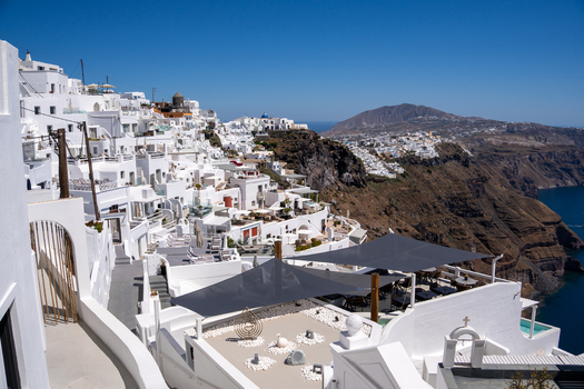 View of white houses and traditional architecture on the volcanic cliffs overlooking the Aegean Sea under a clear blue sky in Fira Greece. View of white houses and traditional architecture on the volcanic cliffs overlooking the Aegean Sea under a clear blue sky in Fira Greece.