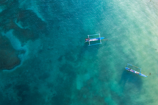 Aerial view of Tanjung Aan Beach with traditional blue outrigger boats floating on crystal clear turquoise water and coral reefs Kecamatan Pujut Nusa Tenggara Barat Indonesia.