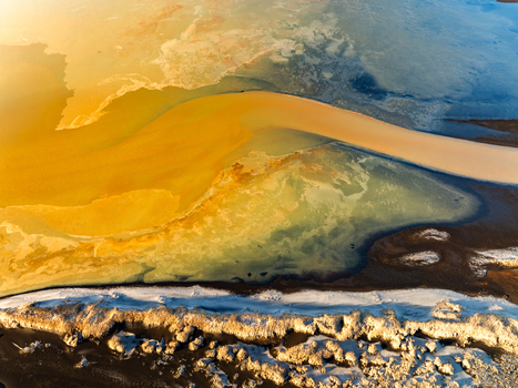 Aerial view of the vibrant yellow and ochre mineral rich geothermal waters contrasting with dark volcanic terrain and patches of snow in Reykjanesbaer Iceland. Aerial view of the vibrant yellow and ochre mineral rich geothermal waters contrasting with dark volcanic terrain and patches of snow in Reykjanesbaer Iceland.