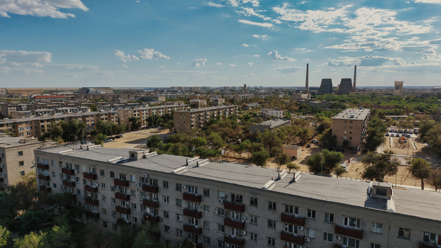 Aerial view of the Baikonur Cosmodrome area featuring residential apartment buildings industrial chimneys and sparse trees under a blue sky in Karmakshy District Kyzylorda Region Kazakhstan.