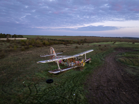 Aerial view of an abandoned graffiti covered biplane resting in a grassy field under a twilight sky in Bulgaria. Aerial view of an abandoned graffiti covered biplane resting in a grassy field under a twilight sky in Bulgaria.