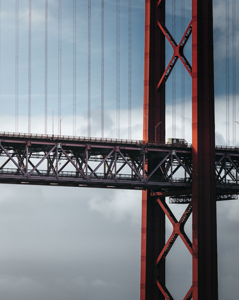 View of iconic red suspension bridge against a cloudy sky Lisbon Portugal.