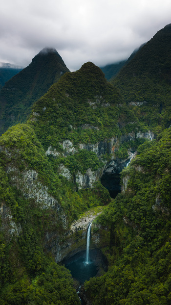 Aerial view of the massive waterfalls cascading down lush green volcanic cliffs in the heart of the tropical forest in La Reunion France. Aerial view of the massive waterfalls cascading down lush green volcanic cliffs in the heart of the tropical forest in La Reunion France.
