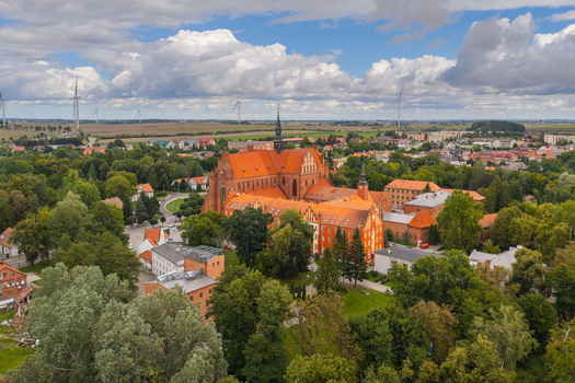 Aerial view of Pelplin Abbey with its red brick Gothic architecture and tiled roofs surrounded by lush greenery and wind turbines in Pelplin Pomeranian Voivodeship Poland. Aerial view of Pelplin Abbey with its red brick Gothic architecture and tiled roofs surrounded by lush greenery and wind turbines in Pelplin Pomeranian Voivodeship Poland.