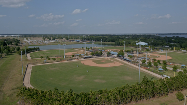 Aerial view of a baseball complex featuring multiple fields with dirt infields and green grass surrounded by trees and a pond in Polk City Florida United States. Aerial view of a baseball complex featuring multiple fields with dirt infields and green grass surrounded by trees and a pond in Polk City Florida United States.