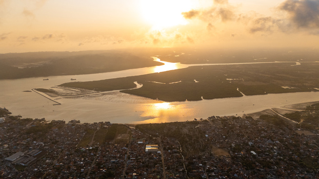 Aerial view of the river mouth and coastal landscape at sunset with golden light reflecting on the water surrounded by urban rooftops and mangrove forests in Cilacap Central Java Indonesia. Aerial view of the river mouth and coastal landscape at sunset with golden light reflecting on the water surrounded by urban rooftops and mangrove forests in Cilacap Central Java Indonesia.