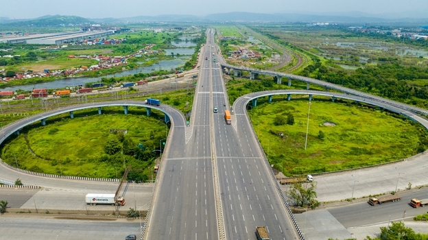Aerial view of the JNPT Interchange featuring multi level highway ramps heavy trucks on the road and lush green surroundings in the industrial landscape of Navi Mumbai Maharashtra India.