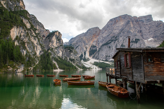 View of wooden boats floating on the emerald waters of Lago di Braies with a rustic wooden boathouse on stilts and the towering peaks of the Dolomites in the background Braies Veneto Italy. View of wooden boats floating on the emerald waters of Lago di Braies with a rustic wooden boathouse on stilts and the towering peaks of the Dolomites in the background Braies Veneto Italy.