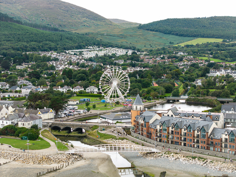 Aerial view of the Ferris wheel in the coastal town of Newcastle featuring buildings a river a bridge and green hills in the background Newcastle Northern Ireland United Kingdom. Aerial view of the Ferris wheel in the coastal town of Newcastle featuring buildings a river a bridge and green hills in the background Newcastle Northern Ireland United Kingdom.