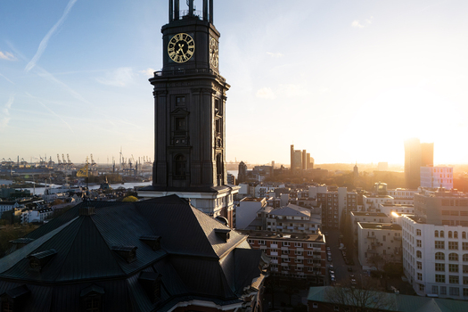 Aerial view of St. Michaeliskirche tower with its golden clock face overlooking urban rooftops and the port cranes during sunset in Hamburg Hamburg Germany.