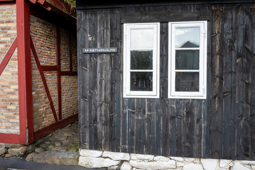 View of a traditional wooden building with black vertical planks white window frames and a stone foundation featuring a small sign on the wall in the Faroe Islands. View of a traditional wooden building with black vertical planks white window frames and a stone foundation featuring a small sign on the wall in the Faroe Islands.