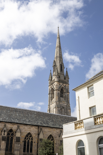 View of the gothic church spire rising above stone walls and historic buildings under a bright blue sky in Newcastle upon Tyne England United Kingdom. View of the gothic church spire rising above stone walls and historic buildings under a bright blue sky in Newcastle upon Tyne England United Kingdom.