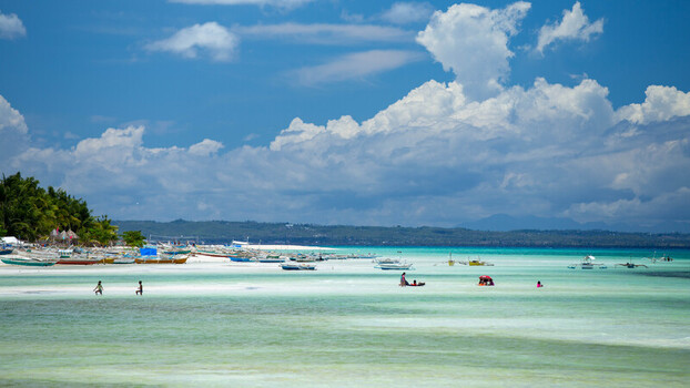 View of Bantayan Island with outrigger boats in shallow turquoise water people wading in the sea under a bright blue sky with fluffy clouds in Cebu Central Visayas Philippines. View of Bantayan Island with outrigger boats in shallow turquoise water people wading in the sea under a bright blue sky with fluffy clouds in Cebu Central Visayas Philippines.