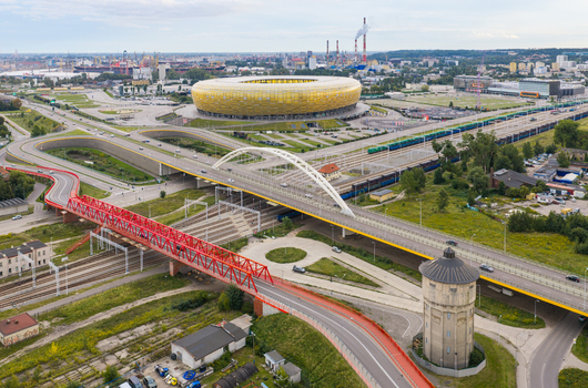 Aerial view of the Polsat Plus Arena Gdansk a yellow gold stadium featuring a modern arched bridge railway tracks and a historic water tower in Gdansk Pomeranian Voivodeship Poland. Aerial view of the Polsat Plus Arena Gdansk a yellow gold stadium featuring a modern arched bridge railway tracks and a historic water tower in Gdansk Pomeranian Voivodeship Poland.
