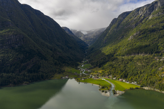 Aerial view of the Sandvinvatnet lake and lush green valley with a winding river and steep mountains under a cloudy sky in Sandvin Vestland Norway. Aerial view of the Sandvinvatnet lake and lush green valley with a winding river and steep mountains under a cloudy sky in Sandvin Vestland Norway.