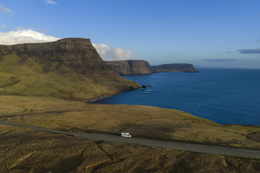 Aerial view of a white camper van parked on a coastal road along dramatic cliffs and the blue sea in Isle of Skye United Kingdom. Aerial view of a white camper van parked on a coastal road along dramatic cliffs and the blue sea in Isle of Skye United Kingdom.