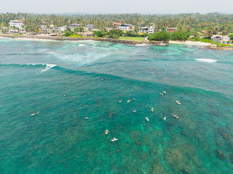 Aerial view of surfers waiting for waves in clear turquoise water near the coastline of Devil s Rock Ahangama Southern Province Sri Lanka. Aerial view of surfers waiting for waves in clear turquoise water near the coastline of Devil s Rock Ahangama Southern Province Sri Lanka.