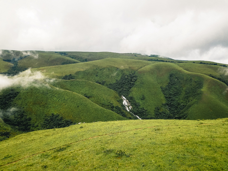 Aerial view of lush verdant rolling hills with a sparkling waterfall cascading amidst dark green foliage and soft mist Obudu Cross River Nigeria.