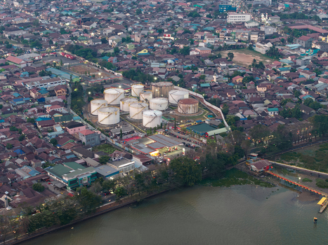 Aerial view of PT. Pertamina TBBM Samarinda fuel storage facility with white tanks near the river surrounded by dense urban housing and rooftops in Samarinda Kalimantan Timur Indonesia.