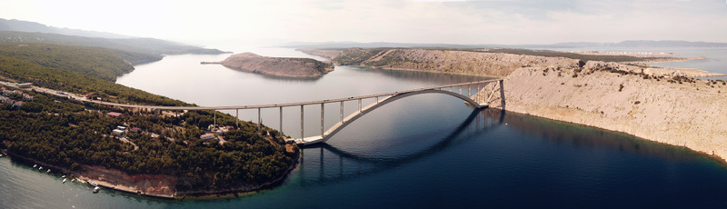 Aerial view of the Krk Bridge spanning the Adriatic Sea connecting the island of Krk to the mainland with its iconic concrete arch surrounded by rugged coastal cliffs in Krk Croatia.
