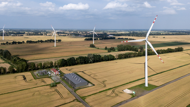 Aerial view of wind turbines standing in golden agricultural fields with a small power substation and a building nearby under a blue sky in Gdansk Pomeranian Voivodeship Poland. Aerial view of wind turbines standing in golden agricultural fields with a small power substation and a building nearby under a blue sky in Gdansk Pomeranian Voivodeship Poland.