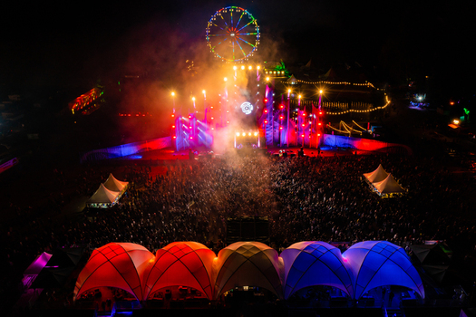 Herzogenaurach Germany 22 July 2022 Aerial view of Open Beatz Festival with a colorful ferris wheel illuminated main stage and a large crowd of people at night. Herzogenaurach Germany 22 July 2022 Aerial view of Open Beatz Festival with a colorful ferris wheel illuminated main stage and a large crowd of people at night.
