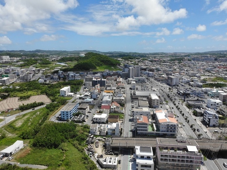 Aerial view of the urban landscape of Haebaru with residential buildings commercial structures and green hills under a blue sky in Haebaru Okinawa Japan.