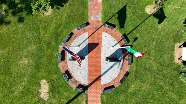 Aerial view of a circular memorial with a brick walkway benches and flags of the United States and Italy set in a grassy park in New Castle Delaware United States.