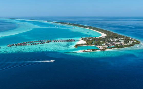 Aerial view of a tropical island resort with overwater bungalows white sandy beaches and a boat cruising in the turquoise lagoon in Kudahuvadhoo Dhaalu Atoll Maldives. Aerial view of a tropical island resort with overwater bungalows white sandy beaches and a boat cruising in the turquoise lagoon in Kudahuvadhoo Dhaalu Atoll Maldives.