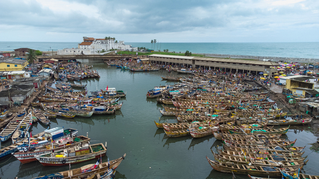 Aerial view of Elmina Castle overlooking a bustling harbor filled with numerous traditional wooden fishing boats in Elmina Central Region Ghana. Aerial view of Elmina Castle overlooking a bustling harbor filled with numerous traditional wooden fishing boats in Elmina Central Region Ghana.
