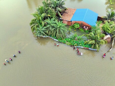 Banshkhali Upazila Bangladesh 10 July 2026 Aerial view of a house surrounded by floodwaters with palm trees and people wading through the water in Chittagong Division. Banshkhali Upazila Bangladesh 10 July 2026 Aerial view of a house surrounded by floodwaters with palm trees and people wading through the water in Chittagong Division.