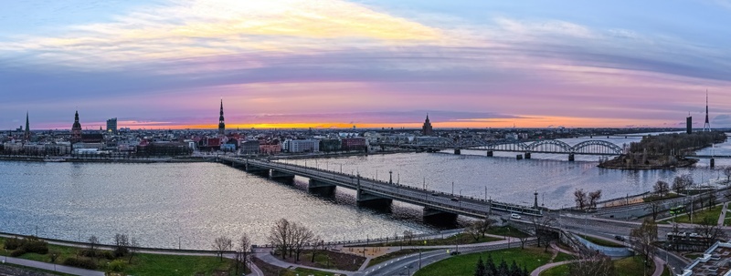 Aerial view of the Riga city skyline featuring the Daugava river historic bridges and church spires under a vibrant sunset sky in Riga Latvia.
