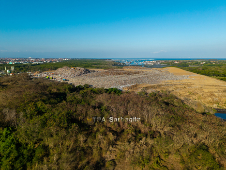 Aerial view of TPA Suwung landfill site with large waste piles surrounded by lush forest and coastal scenery in Kecamatan Denpasar Selatan Bali Indonesia.