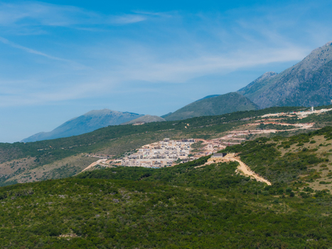 Aerial view of a hillside construction site with white buildings surrounded by lush green vegetation and rugged mountains in Jala Vlore County Albania. Aerial view of a hillside construction site with white buildings surrounded by lush green vegetation and rugged mountains in Jala Vlore County Albania.