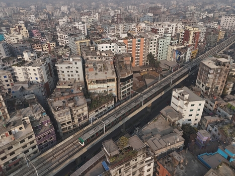 Aerial view of the Dhaka Metro Rail train traveling on an elevated track through the dense urban landscape featuring residential buildings in Dhaka Dhaka Division Bangladesh. Aerial view of the Dhaka Metro Rail train traveling on an elevated track through the dense urban landscape featuring residential buildings in Dhaka Dhaka Division Bangladesh.