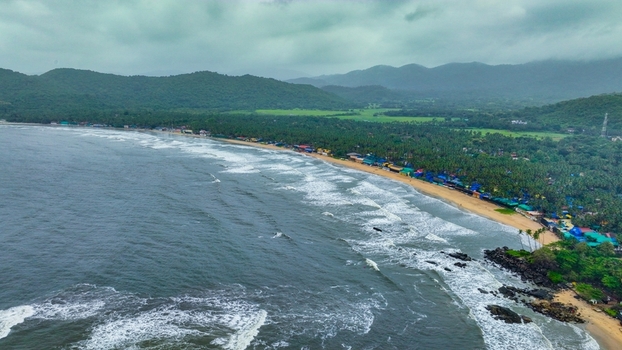 Aerial view of Palolem Beach with its crescent shaped coastline lush palm trees and rolling hills under a cloudy sky in Canacona Goa India.