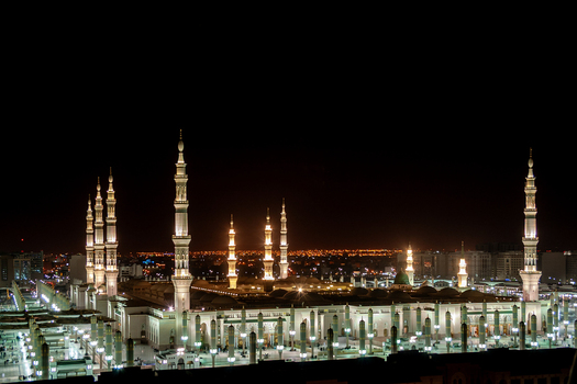 View of the illuminated Al Masjid e Nabawi with its towering minarets and domes glowing against the night sky in Madinah Al Madinah Province Saudi Arabia.