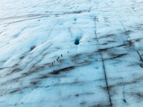 Aerial view of Breidamerkurjokull glacier with hikers walking across blue ice marked by dark volcanic ash streaks and deep crevasses in Sveitarfelagid Hornafjordur Iceland. Aerial view of Breidamerkurjokull glacier with hikers walking across blue ice marked by dark volcanic ash streaks and deep crevasses in Sveitarfelagid Hornafjordur Iceland.