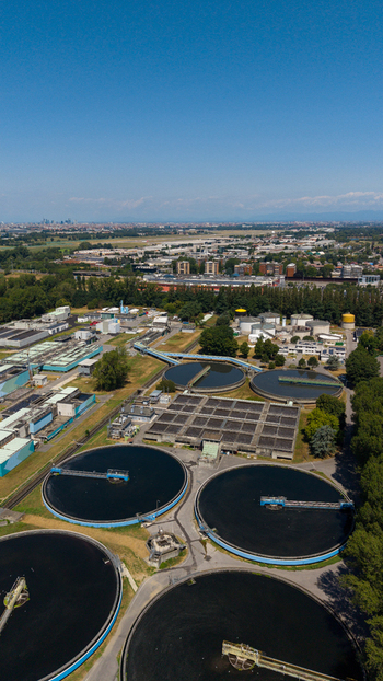 Aerial view of a wastewater treatment plant featuring large circular sedimentation tanks and rectangular basins surrounded by trees and urban infrastructure in Milan Lombardy Italy. Aerial view of a wastewater treatment plant featuring large circular sedimentation tanks and rectangular basins surrounded by trees and urban infrastructure in Milan Lombardy Italy.