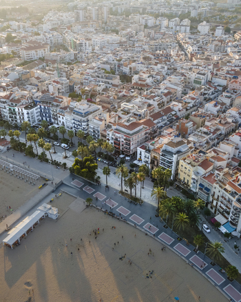 Aerial view of the coastal town of Sitges with its sandy beach palm lined promenade and dense urban architecture under warm sunlight in Sitges Catalonia Spain. Aerial view of the coastal town of Sitges with its sandy beach palm lined promenade and dense urban architecture under warm sunlight in Sitges Catalonia Spain.