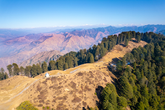 Aerial view of the Chakrata hill station featuring a small temple on a mountain ridge surrounded by pine forests and distant Himalayan peaks in Chakrata Uttarakhand India. Aerial view of the Chakrata hill station featuring a small temple on a mountain ridge surrounded by pine forests and distant Himalayan peaks in Chakrata Uttarakhand India.