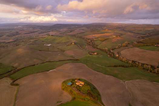 Aerial view of the rolling hills of the Crete Senesi landscape with a farmhouse on a hill during golden hour in Asciano Tuscany Italy.