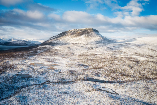 Aerial view of the iconic Saana mountain rising above the snow covered tundra landscape with scattered small lakes and sparse vegetation in Kilpisjarvi Lapland Finland. Aerial view of the iconic Saana mountain rising above the snow covered tundra landscape with scattered small lakes and sparse vegetation in Kilpisjarvi Lapland Finland.